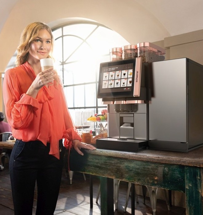 Frau trinkt Latte Macchiato am Bevero Kaffeevollautomat Schaerer Coffee Soul 10